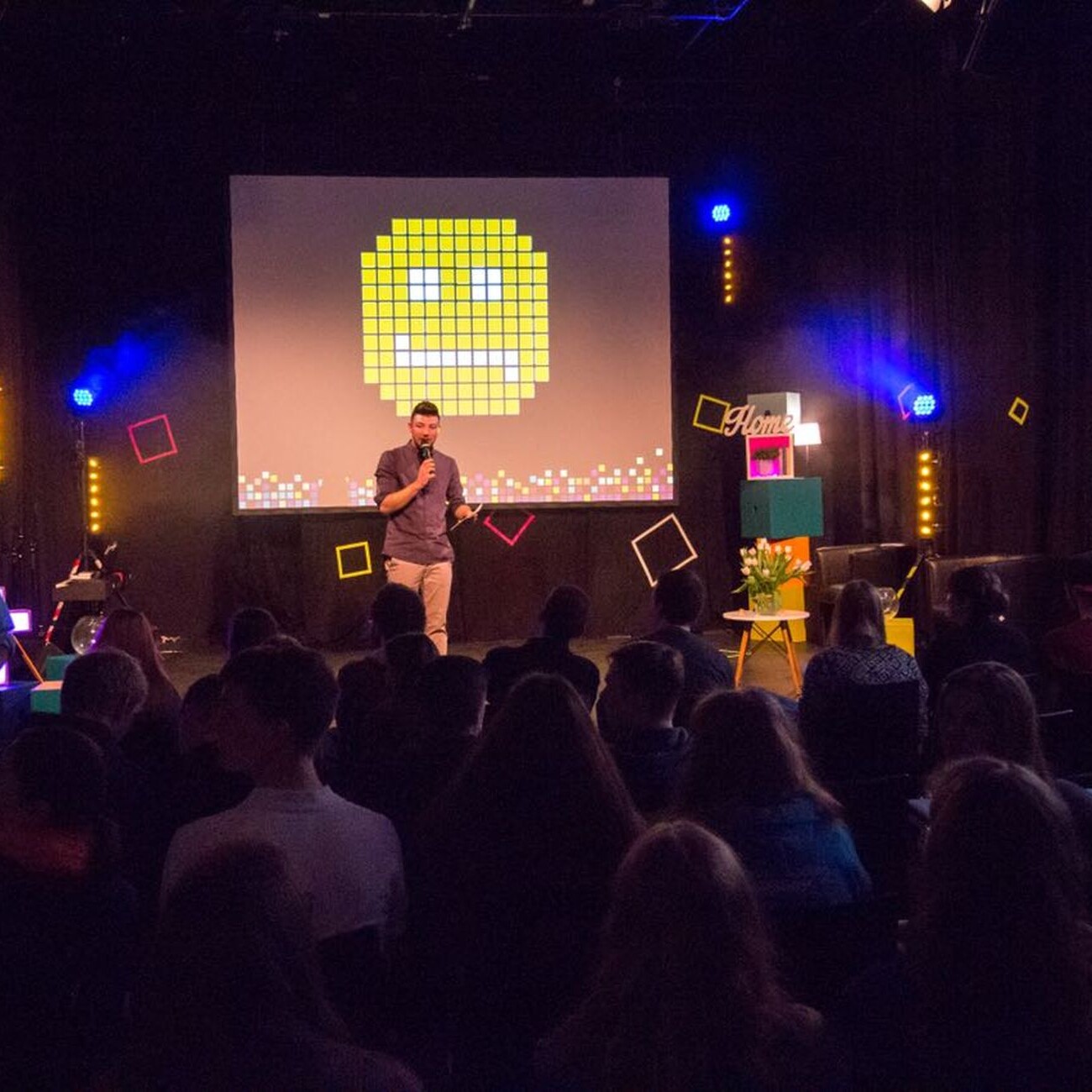 Forum 2018: Redner auf der Bühne vor Publikum. Pixel-Grafik im Hintergrund. Konferenz-Atmosphäre.