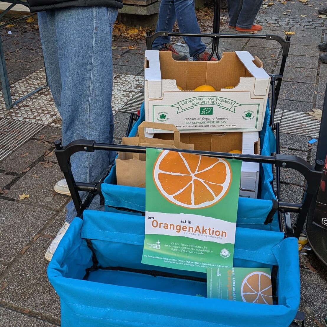 Orangenaktion 2024: Solidarität zeigen. Wagen mit Orangen und Info-Material. Spende für Kinder.