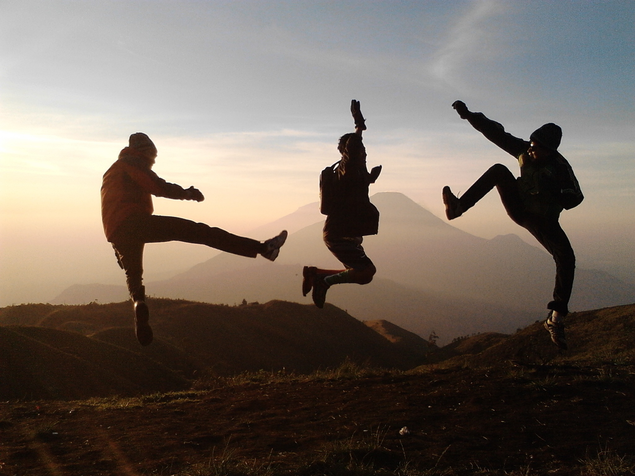 Bergwanderung Spaß: Silhouetten von drei springenden Personen. Wanderer beim Wandern in den Bergen bei Sonnenaufgang.